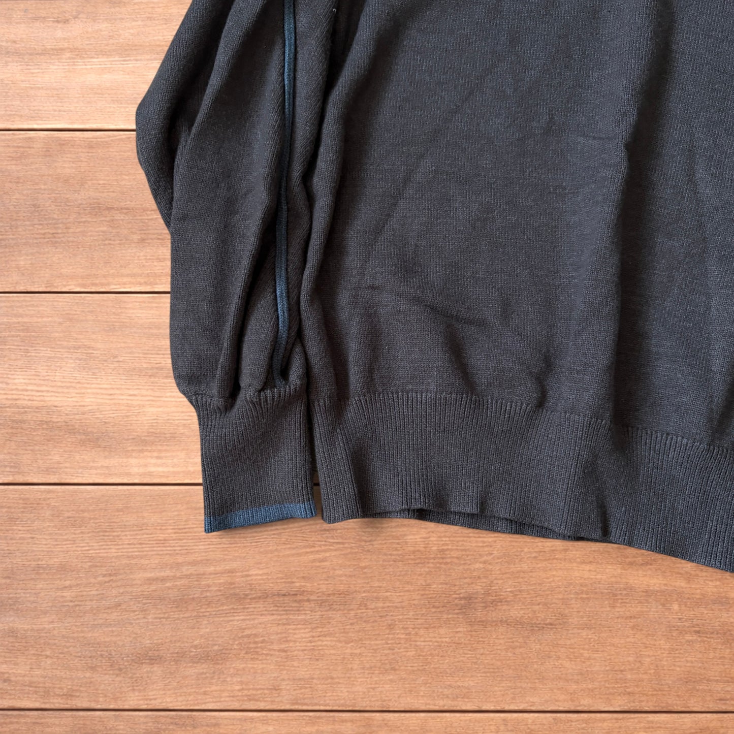 Dark grey vintage style pullover jumper with slim blue piping detail on sleeves laid flat on wooden surface.