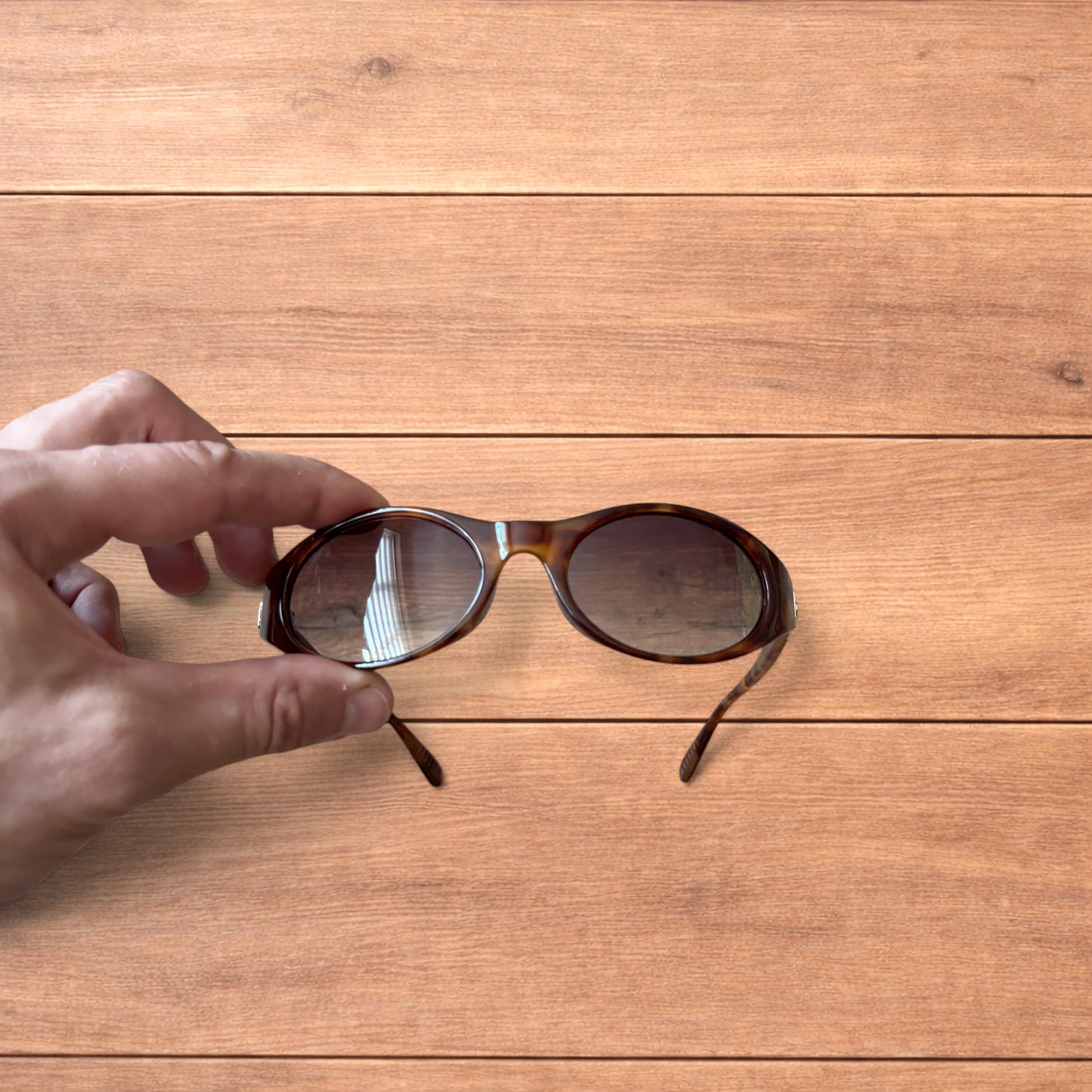 Vintage style tortoiseshell sunglasses with brown lenses held against a wooden background.