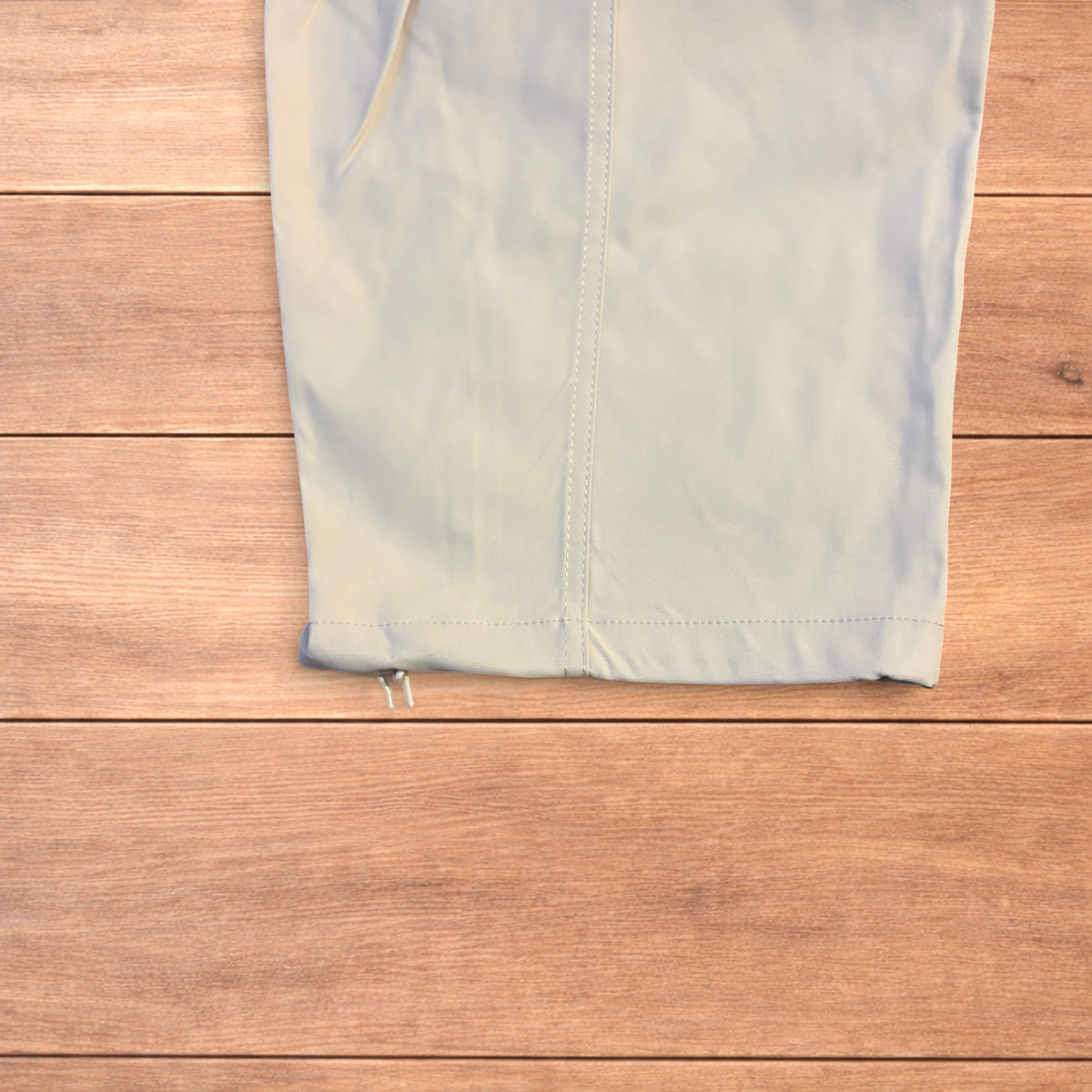 Beige baggy gorpcore hiking pants laid flat showing drawstring waist, toggled hems and back flap pockets.