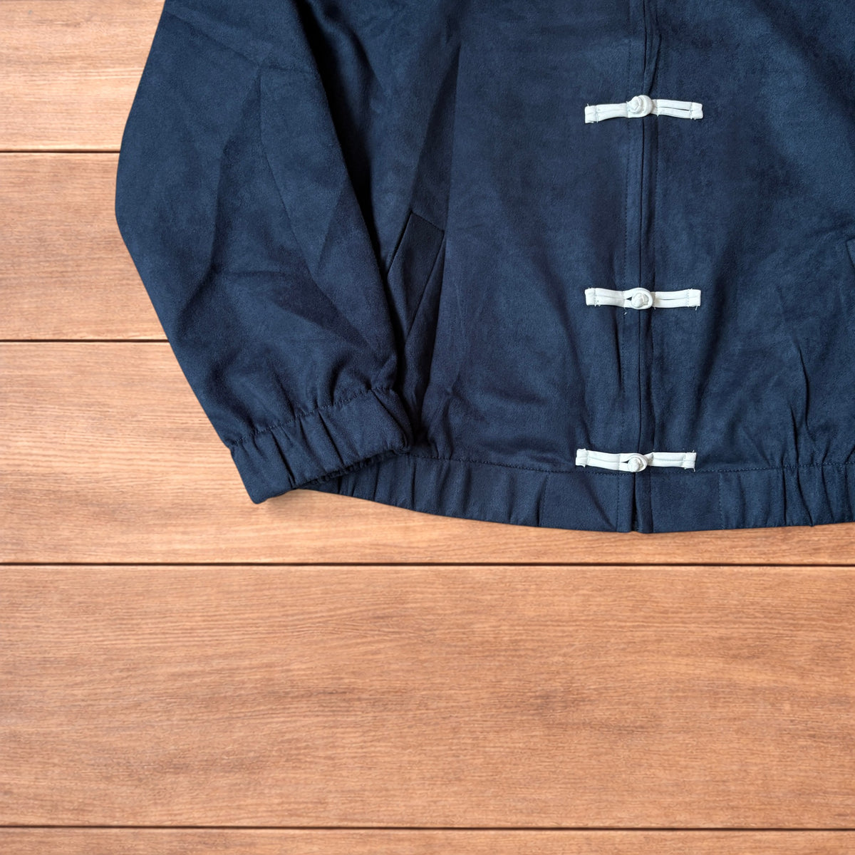 Japanese style navy blue zip up track jacket with white knotted fastenings on wooden background.