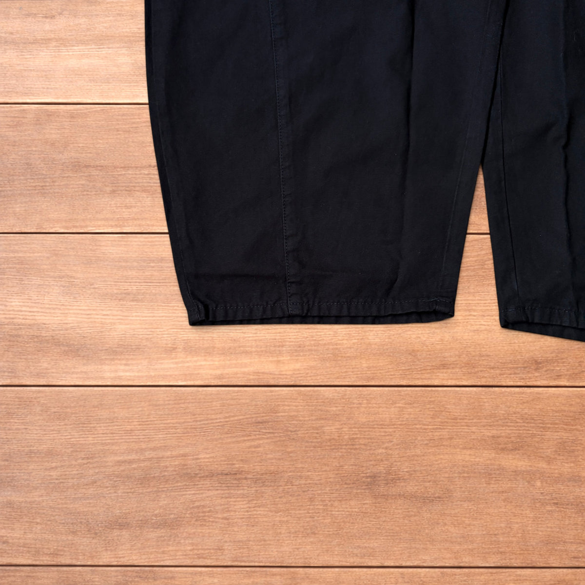 Black baggy balloon chinos laid flat on wooden surface showing wide balloon leg and elasticated hems.