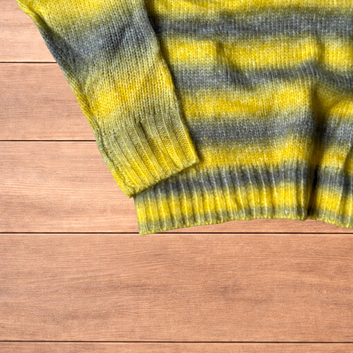 Vintage style baggy knitted sweater jumper with yellow and grey stripes laid flat on wooden surface.