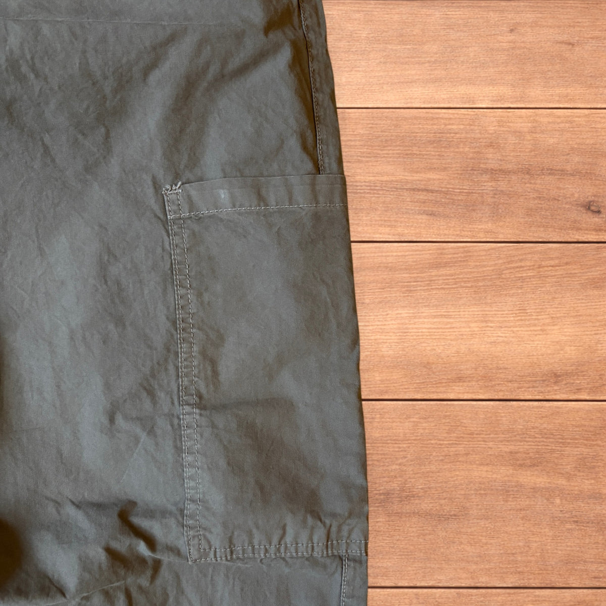 Grey baggy wide leg ripstop cargo trousers with cargo pockets, elasticated waistband and toggled hems laid flat on wooden floor.