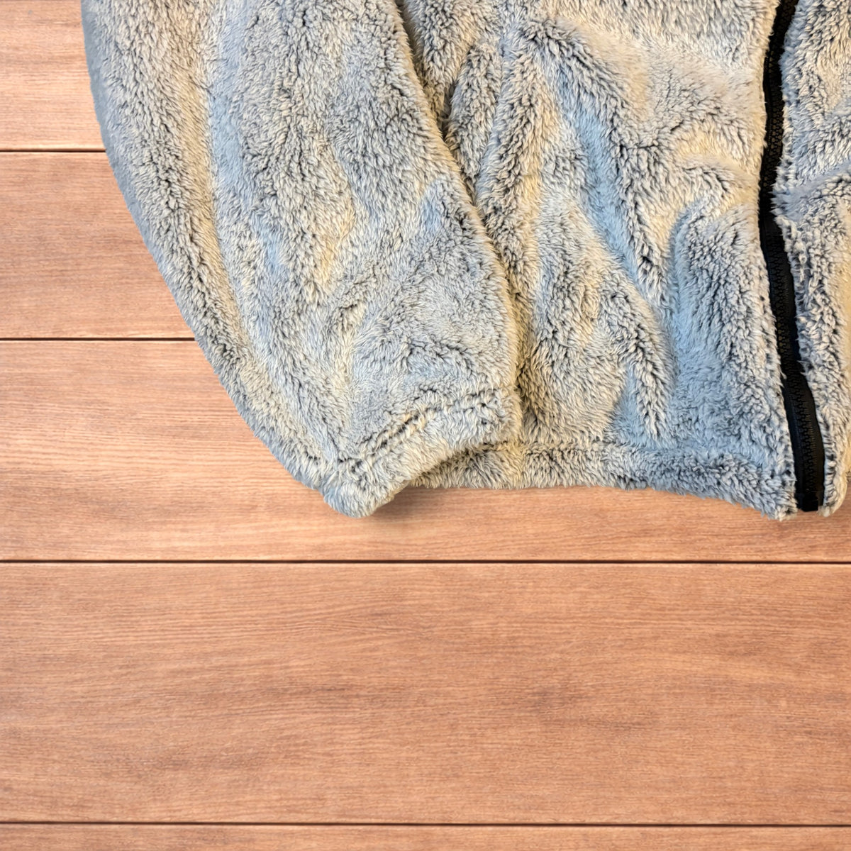 Light grey fluffy zip up hoodie jacket with full zip and hood displayed on wooden floor background