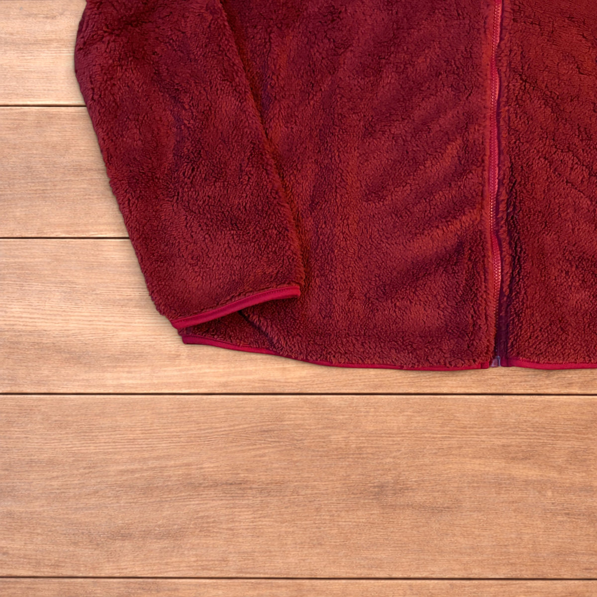 Deep dark red fluffy fleece zip up jacket laid flat on wooden surface.