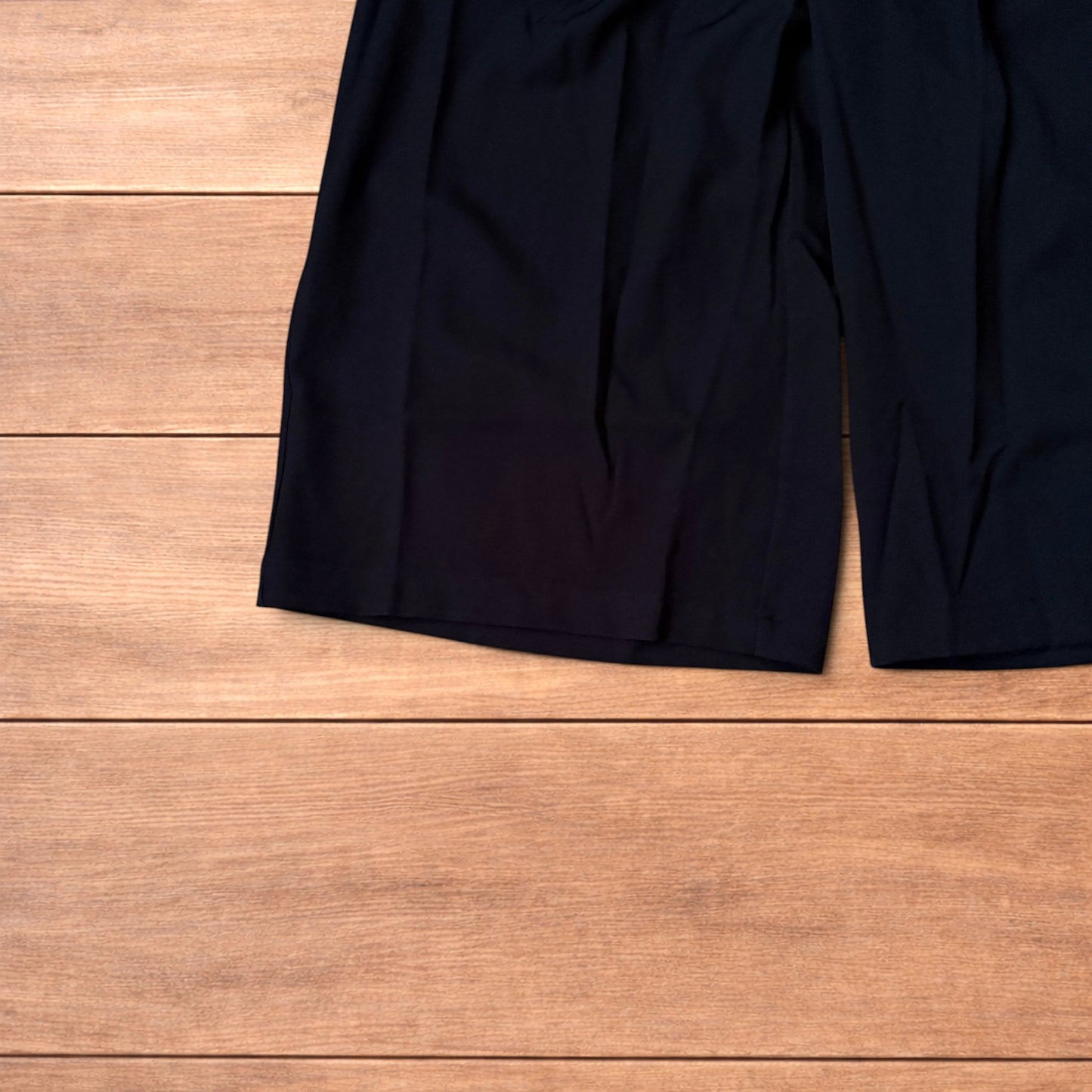 Black vintage style baggy wide leg tailored shorts laid flat on wooden floor showing front and back views