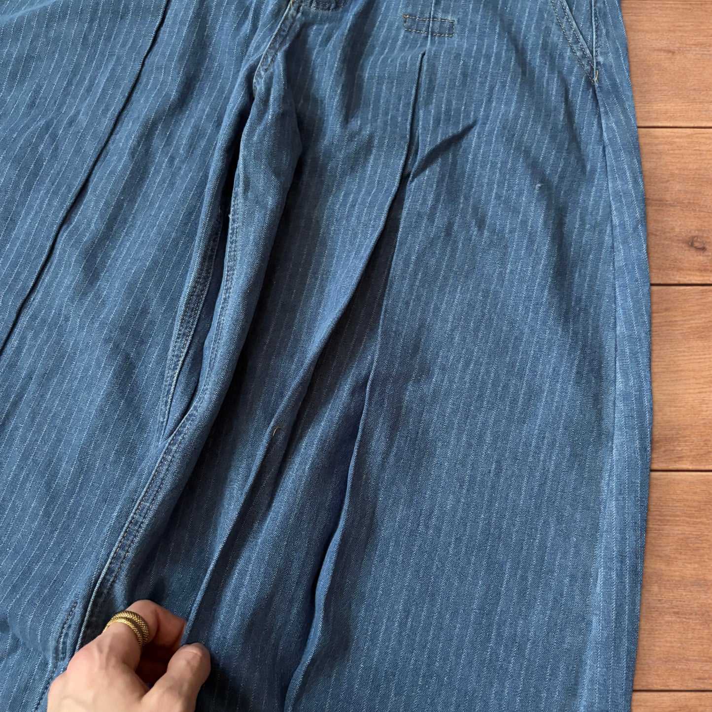 Vintage mid blue pinstripe baggy wide leg jeans with pleats laid flat on wooden surface