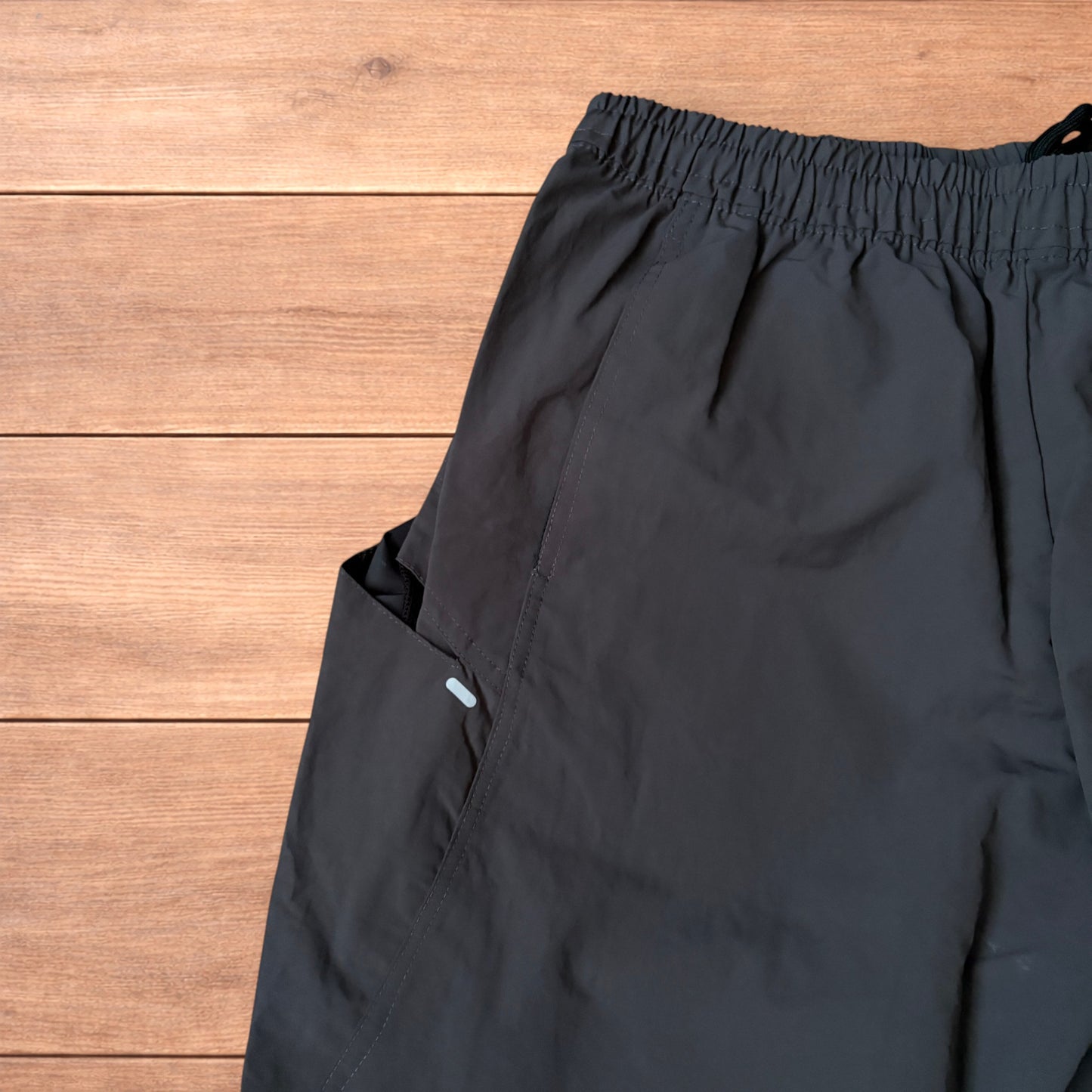 Grey baggy hiking trousers laid flat showing elasticated waistband and side pockets with branding