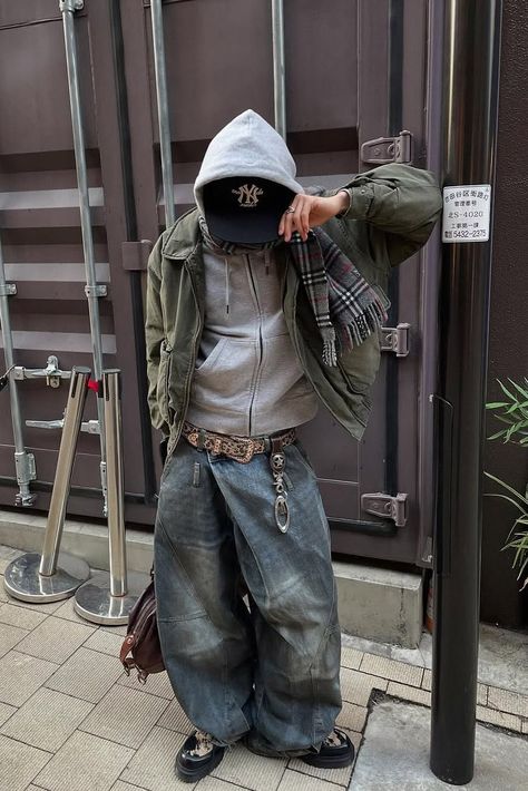 Figure in layered streetwear with jacket, hoodie, baggy jeans and accessories. 