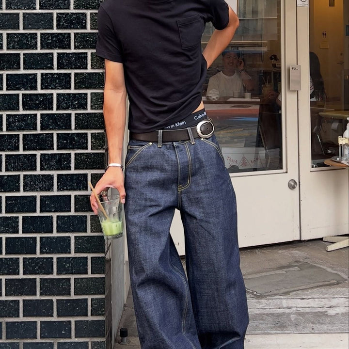 Man in baggy jeans with slim boxy fit top holding a drink.