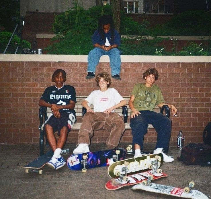 Group of skateborading teens sitting on a bench with their boards displayed in front of them.