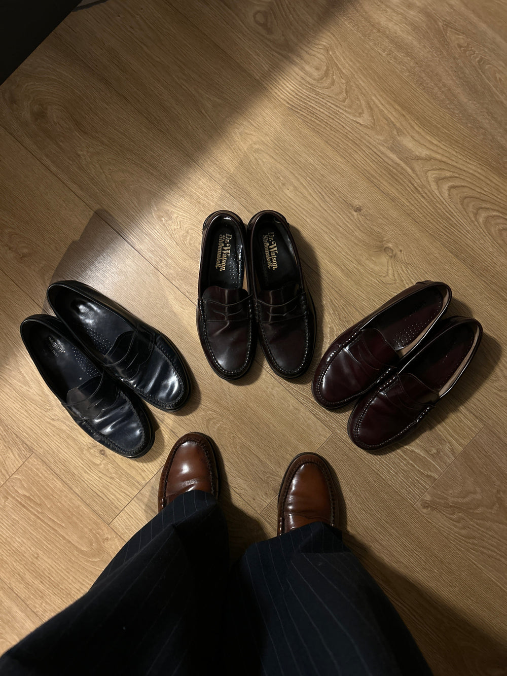 An above view of a figure in pinstripe trousers and loafers with an arrangement of loafers below.