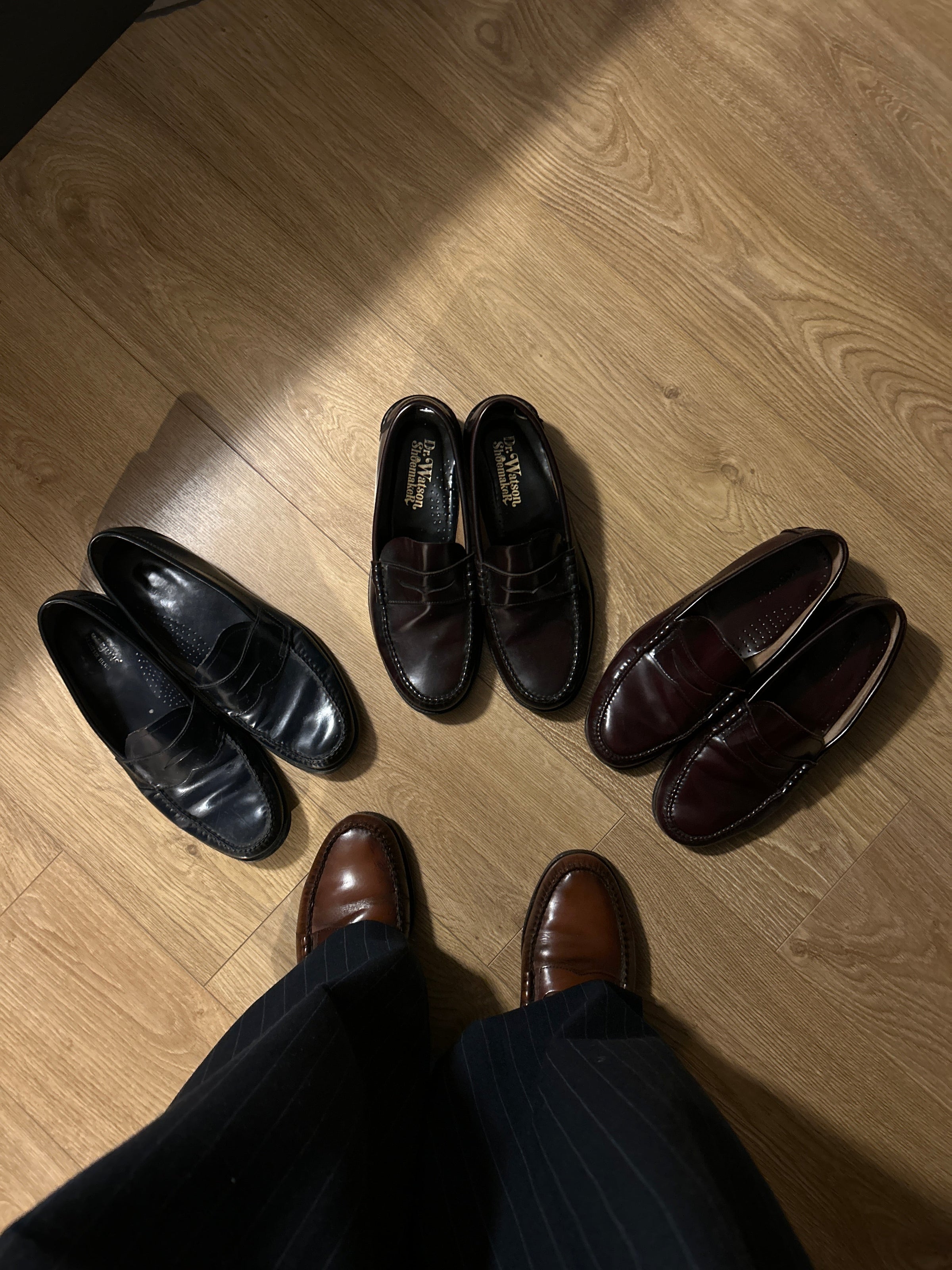 An above view of a figure in pinstripe trousers and loafers with an arrangement of loafers below.