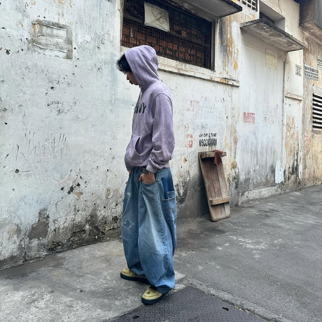 Guy in baggy jeans with boxy hoodie on run down street.