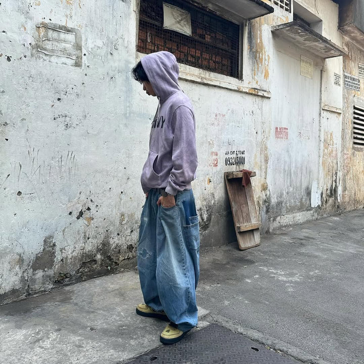 Guy in baggy jeans with boxy hoodie on run down street.