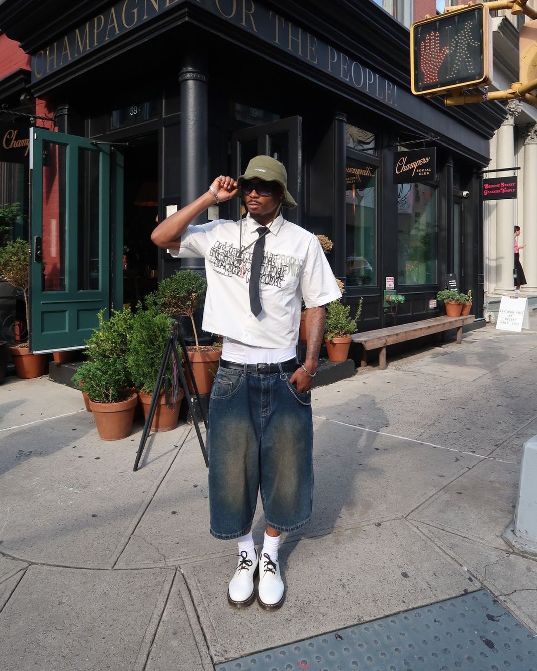 Guy in street wearing summer jorts, shirt and bucket hat with sunglasses.