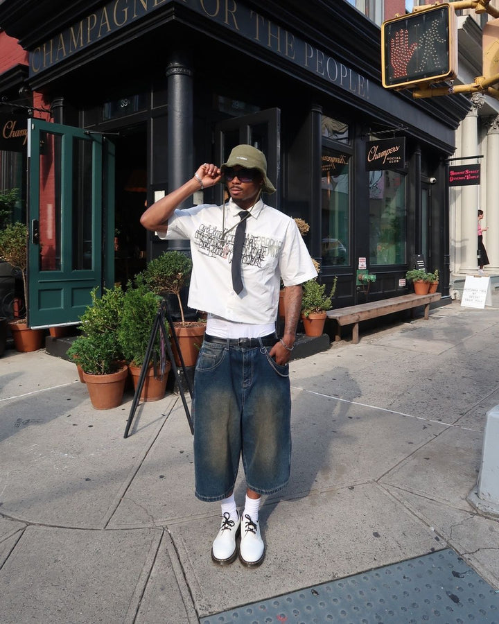 Guy in street wearing summer jorts, shirt and bucket hat with sunglasses.