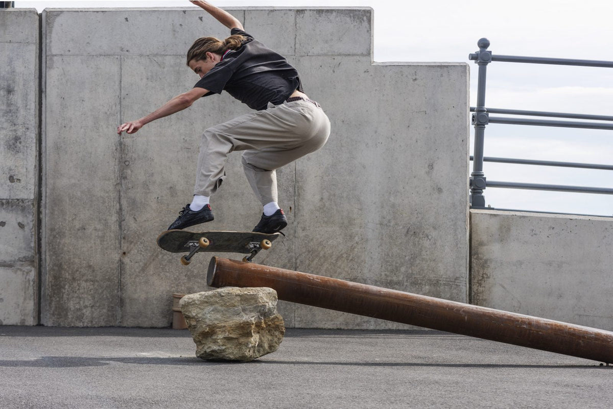 Skateboarder performing a trick over a metal rail against a concrete wall.