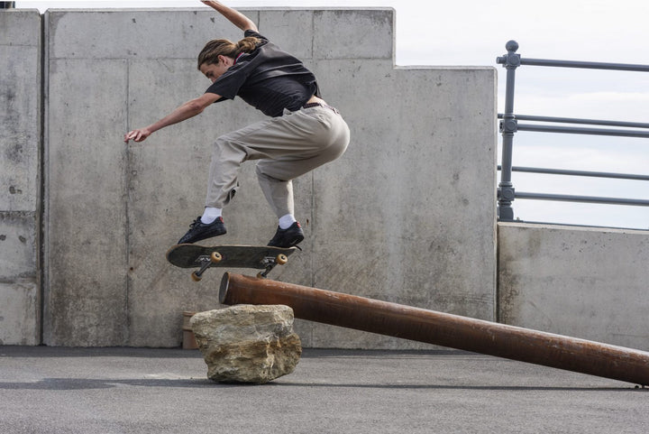 Skateboarder performing a trick over a metal rail against a concrete wall.