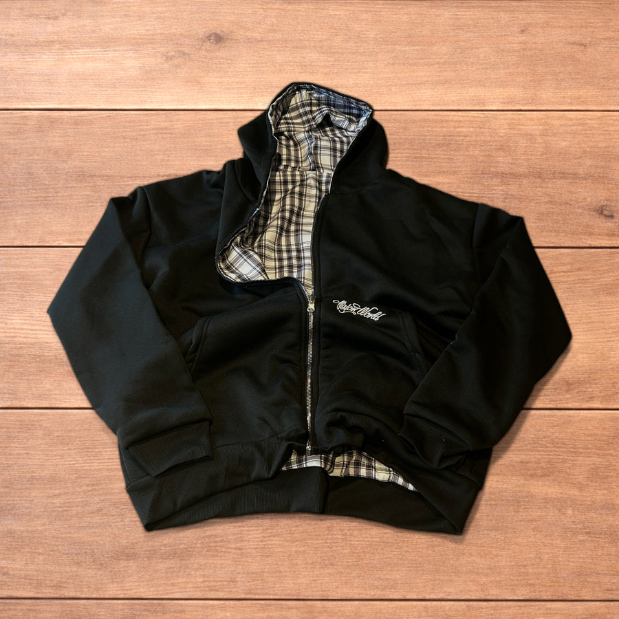 Oversized baggy reversible zip up hoodie jumper with one black side and one grey white checkered side laid flat on wooden surface