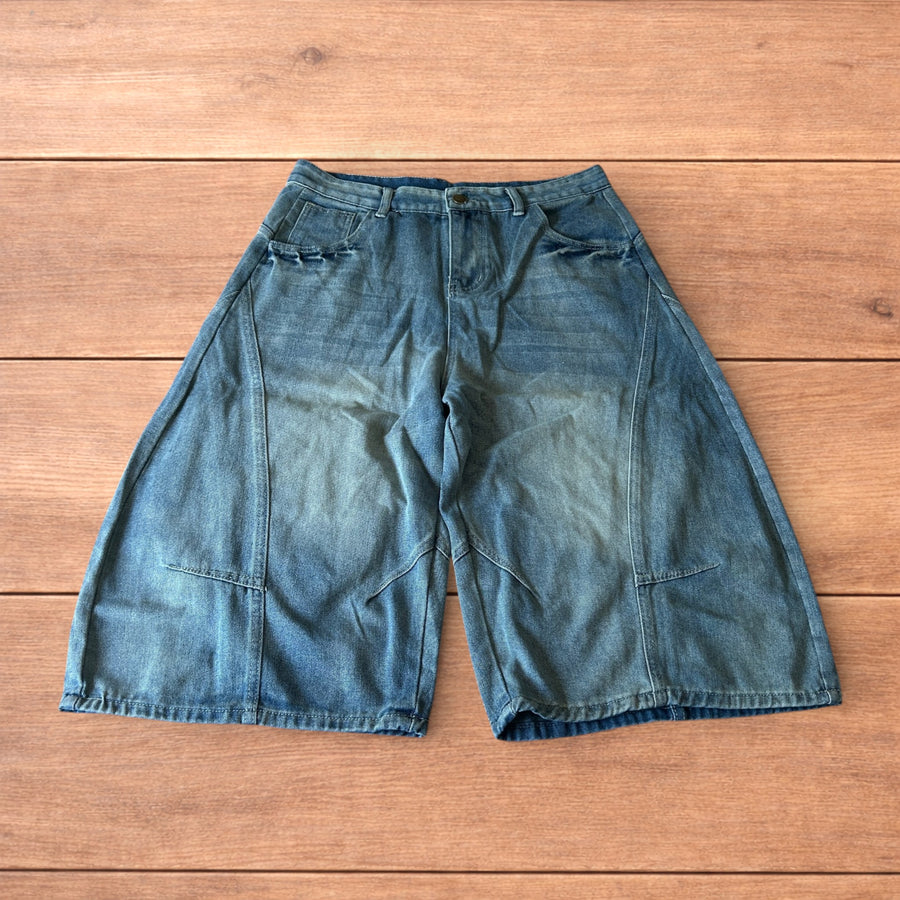 Baggy wide leg mid blue wash denim carpenter shorts with carpenter pockets laid flat on wood