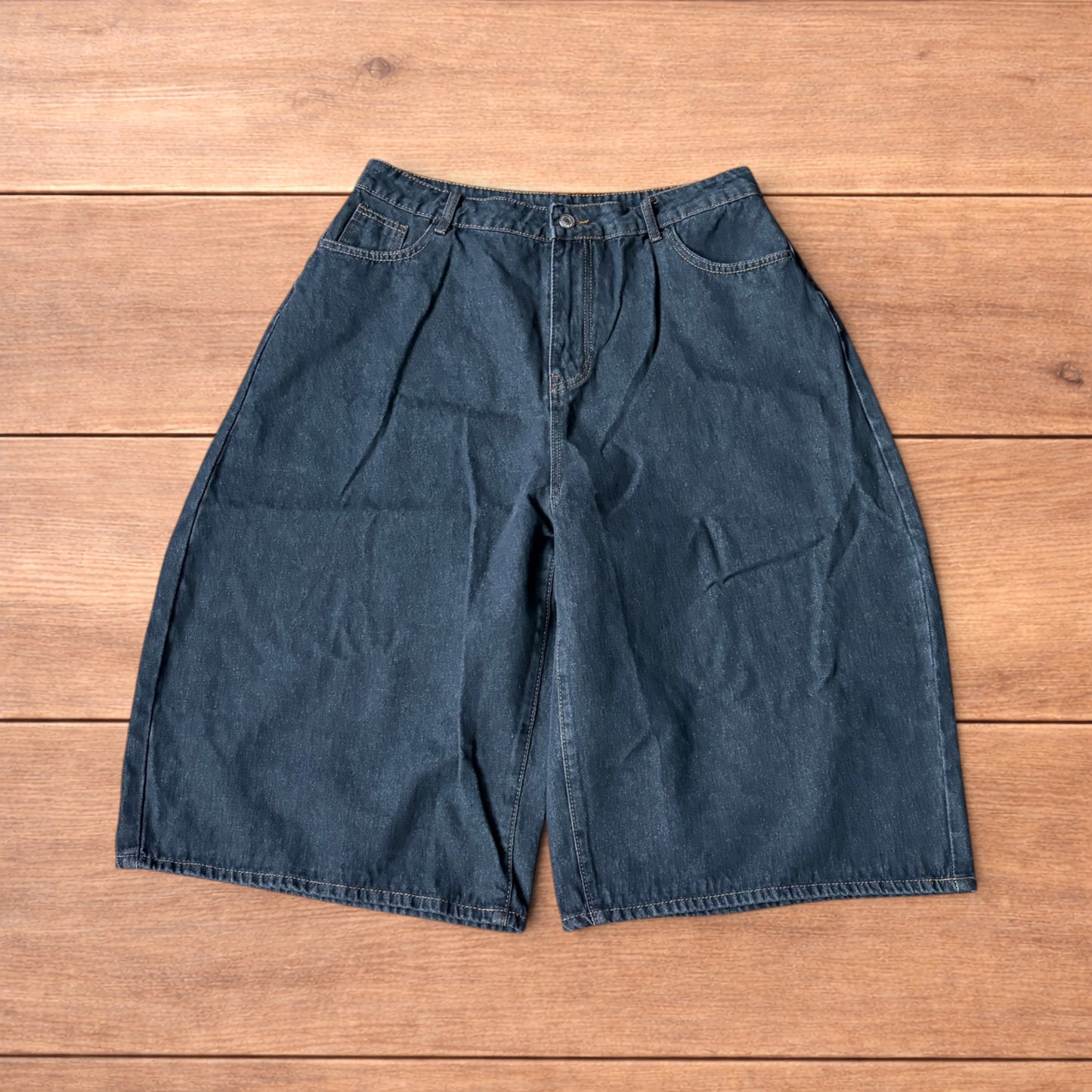 Baggy wide leg denim jorts in washed black with contrast stitching laid flat on wooden surface showing front and back views