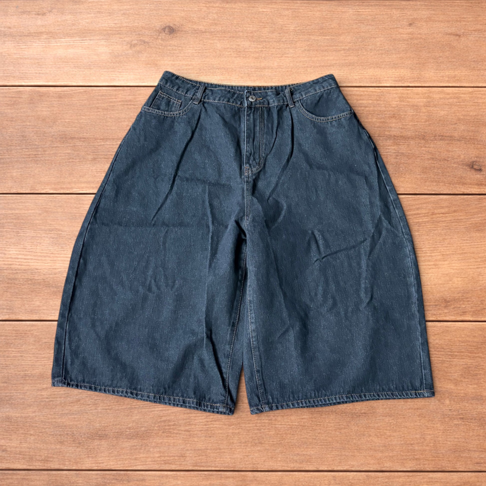 Baggy wide leg denim jorts in washed black with contrast stitching laid flat on wooden surface showing front and back views