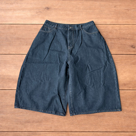 Baggy wide leg denim jorts in washed black with contrast stitching laid flat on wooden surface showing front and back views
