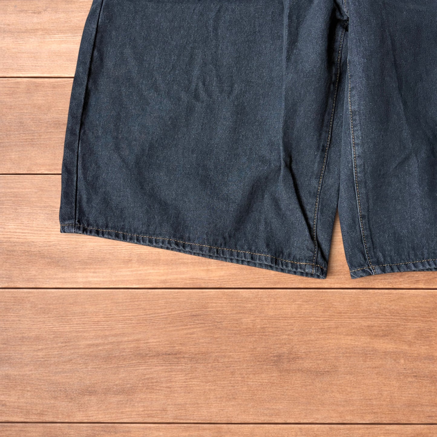 Baggy wide leg denim jorts in washed black with contrast stitching laid flat on wooden surface showing front and back views
