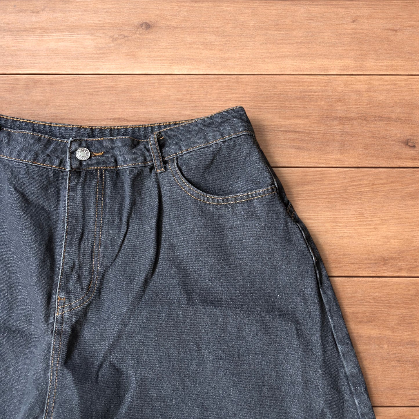 Baggy wide leg denim jorts in washed black with contrast stitching laid flat on wooden surface showing front and back views