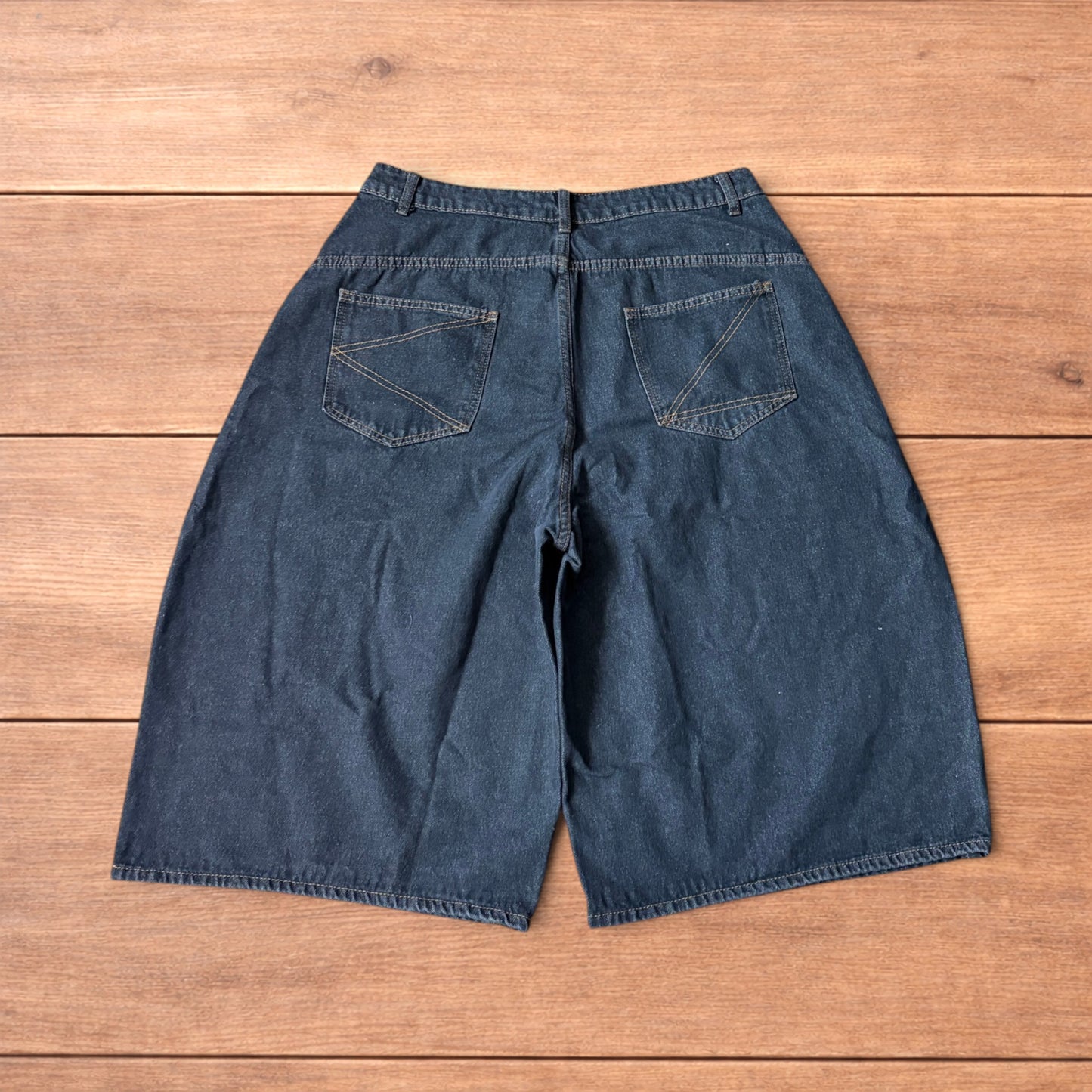 Baggy wide leg denim jorts in washed black with contrast stitching laid flat on wooden surface showing front and back views