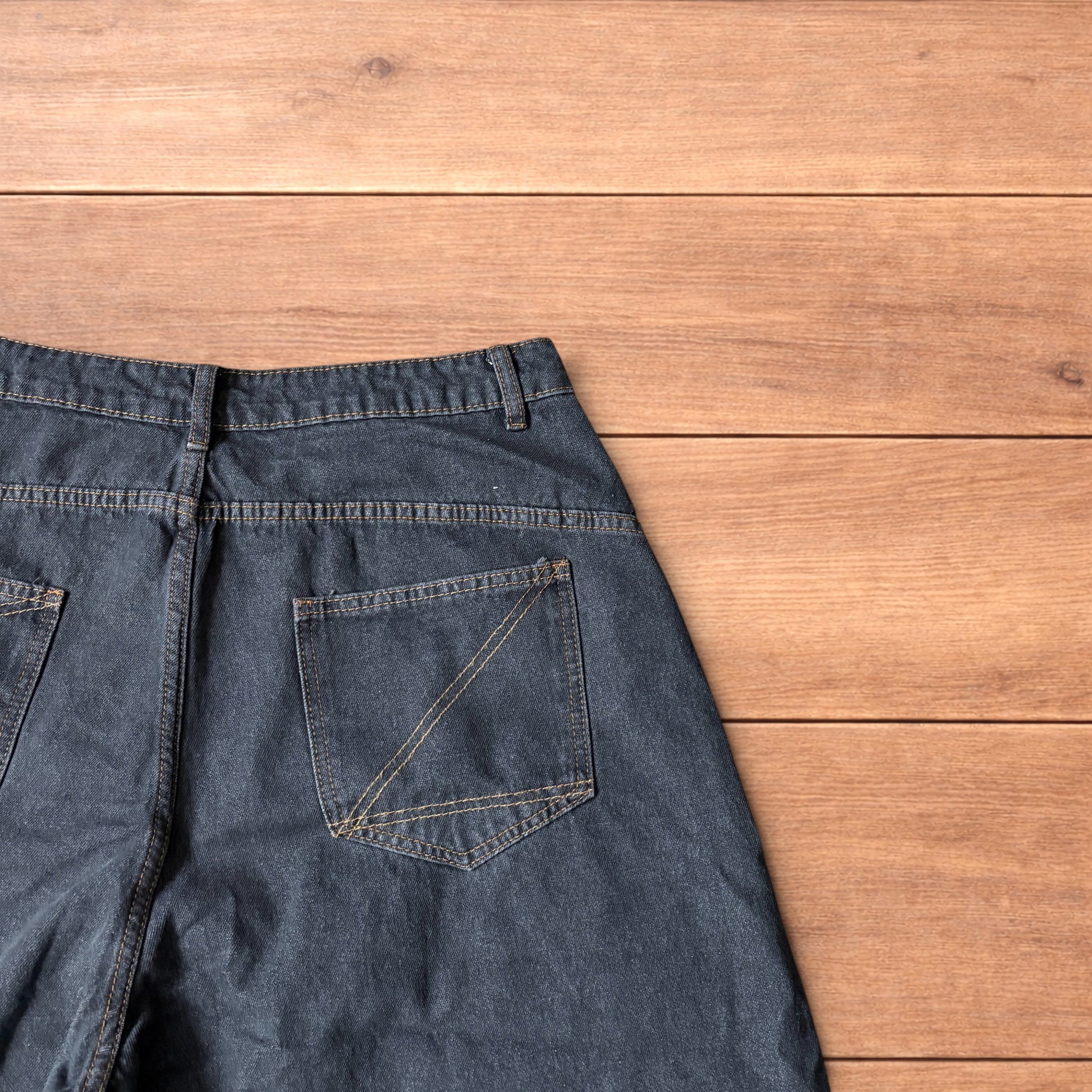 Baggy wide leg denim jorts in washed black with contrast stitching laid flat on wooden surface showing front and back views