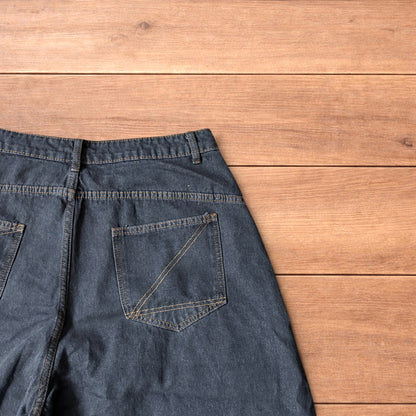 Baggy wide leg denim jorts in washed black with contrast stitching laid flat on wooden surface showing front and back views