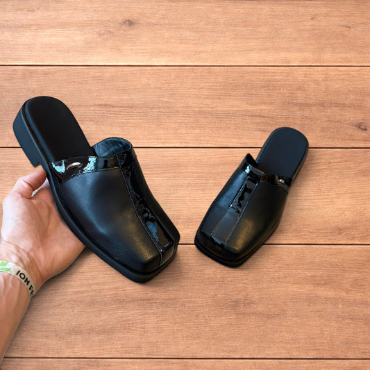 Pair of black faux leather slip on clogs with matte and patent panels and rubber heels on wooden floor