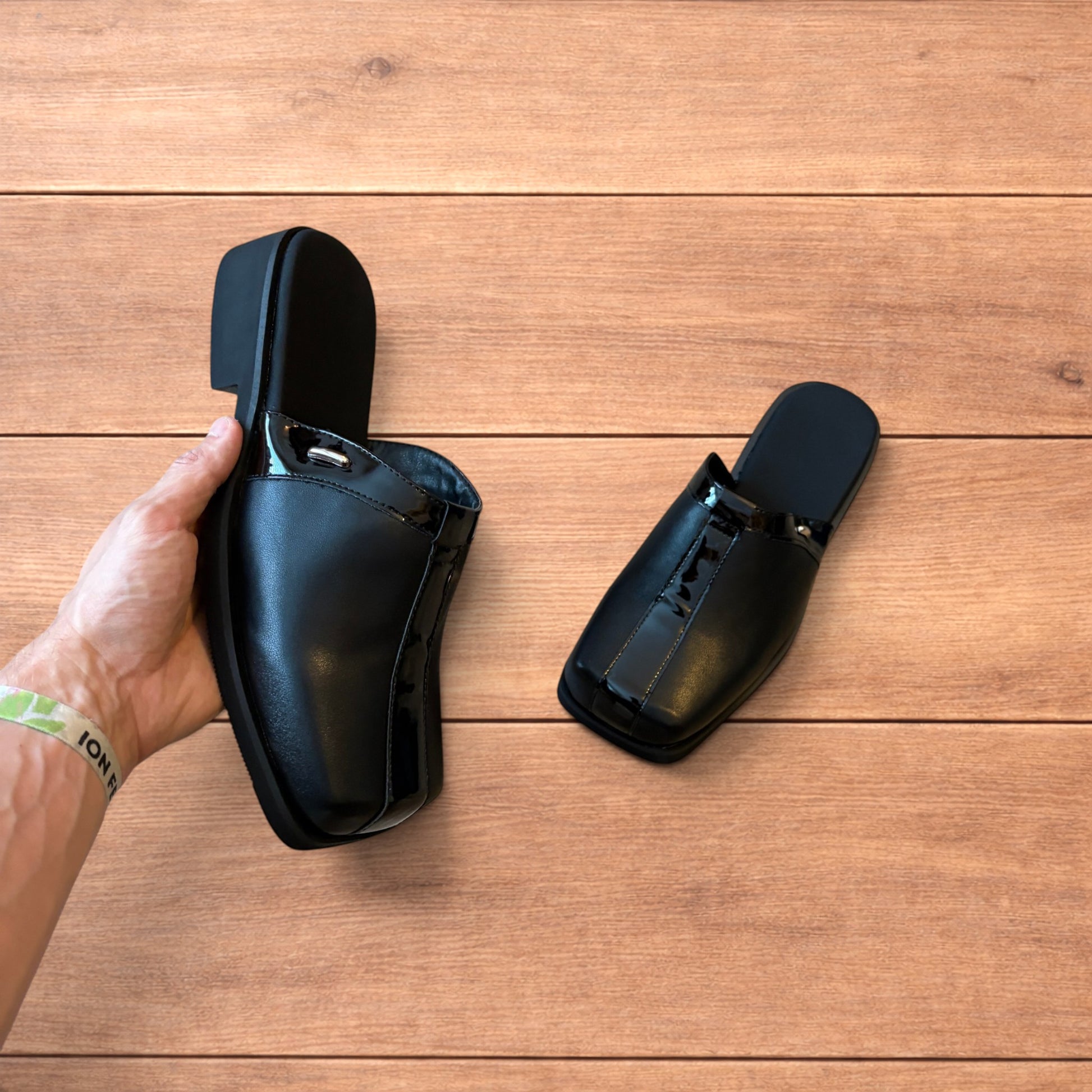 Pair of black faux leather slip on clogs with matte and patent panels and rubber heels on wooden floor