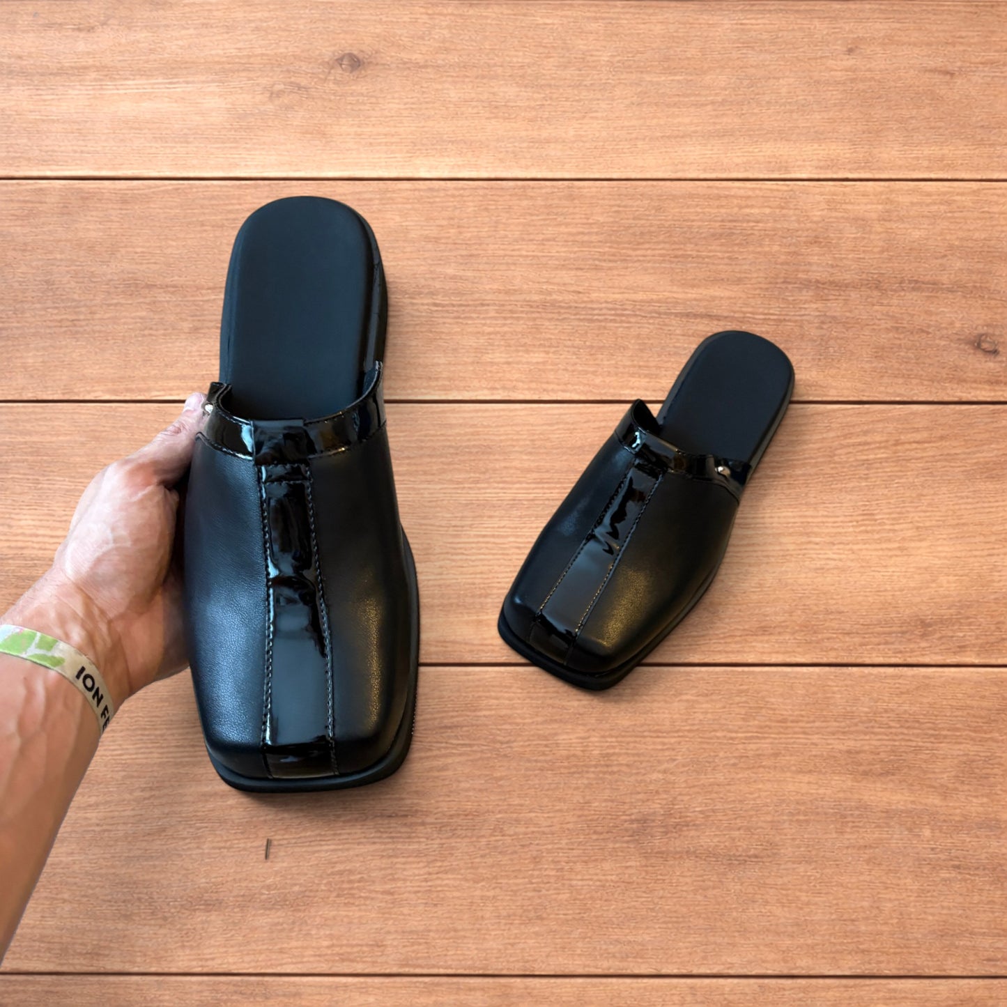 Pair of black faux leather slip on clogs with matte and patent panels and rubber heels on wooden floor