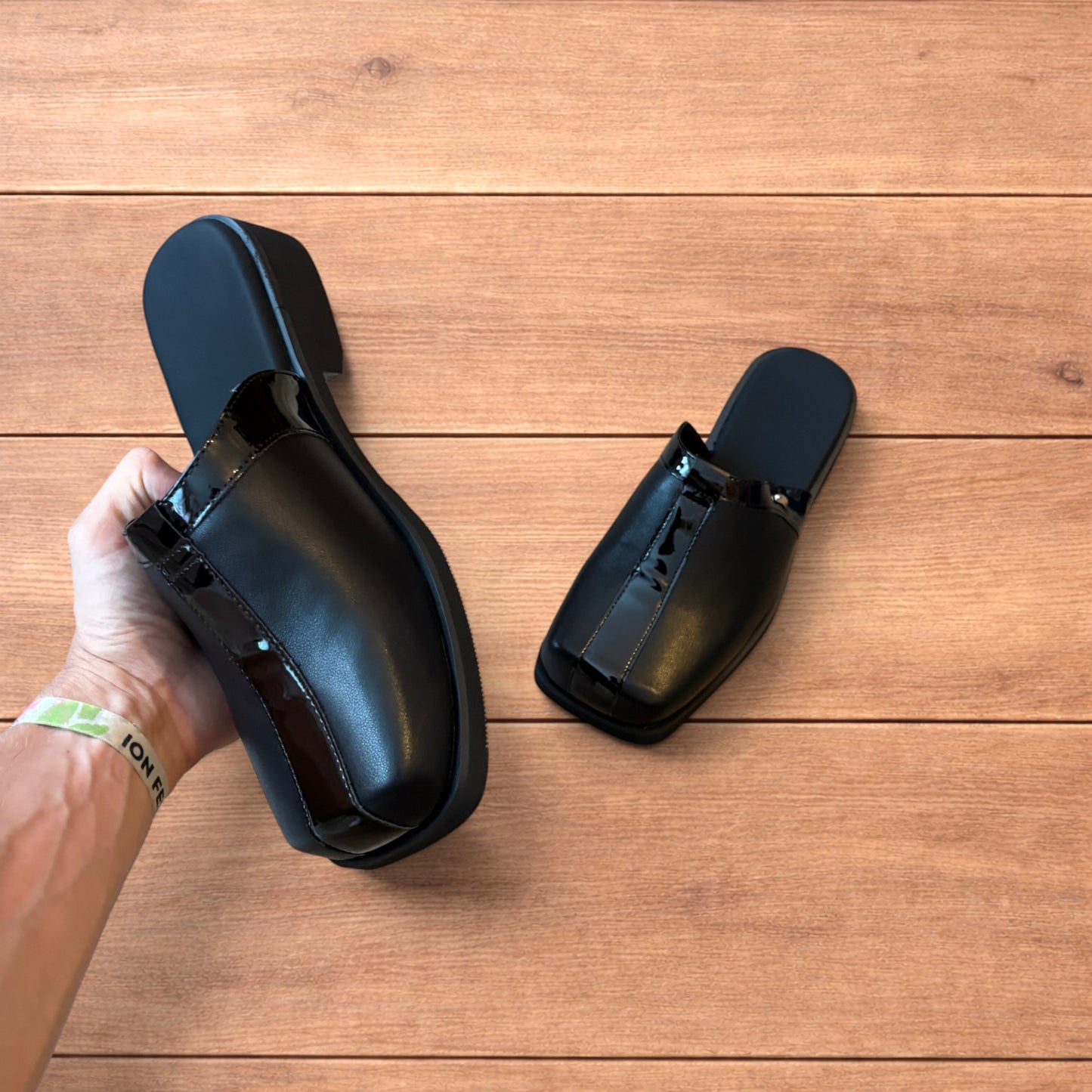 Pair of black faux leather slip on clogs with matte and patent panels and rubber heels on wooden floor