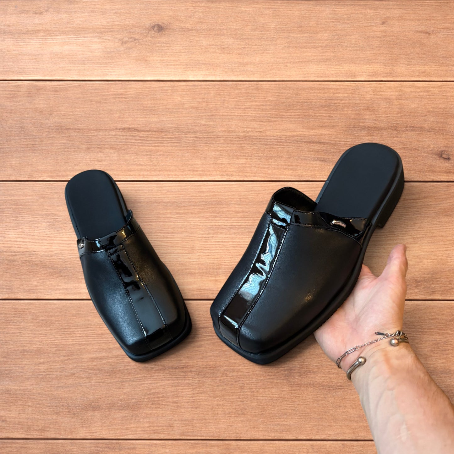 Pair of black faux leather slip on clogs with matte and patent panels and rubber heels on wooden floor