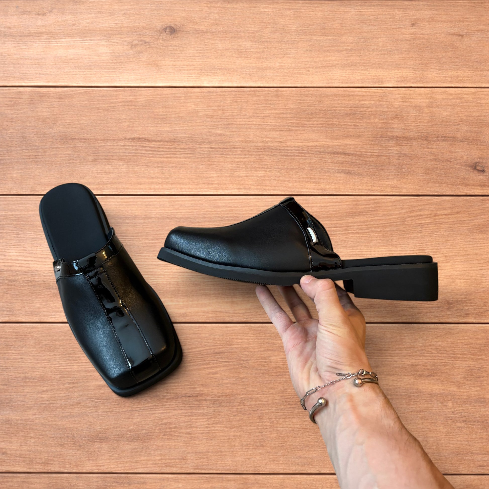 Pair of black faux leather slip on clogs with matte and patent panels and rubber heels on wooden floor