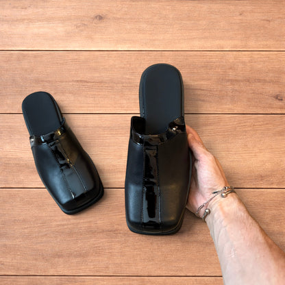 Pair of black faux leather slip on clogs with matte and patent panels and rubber heels on wooden floor