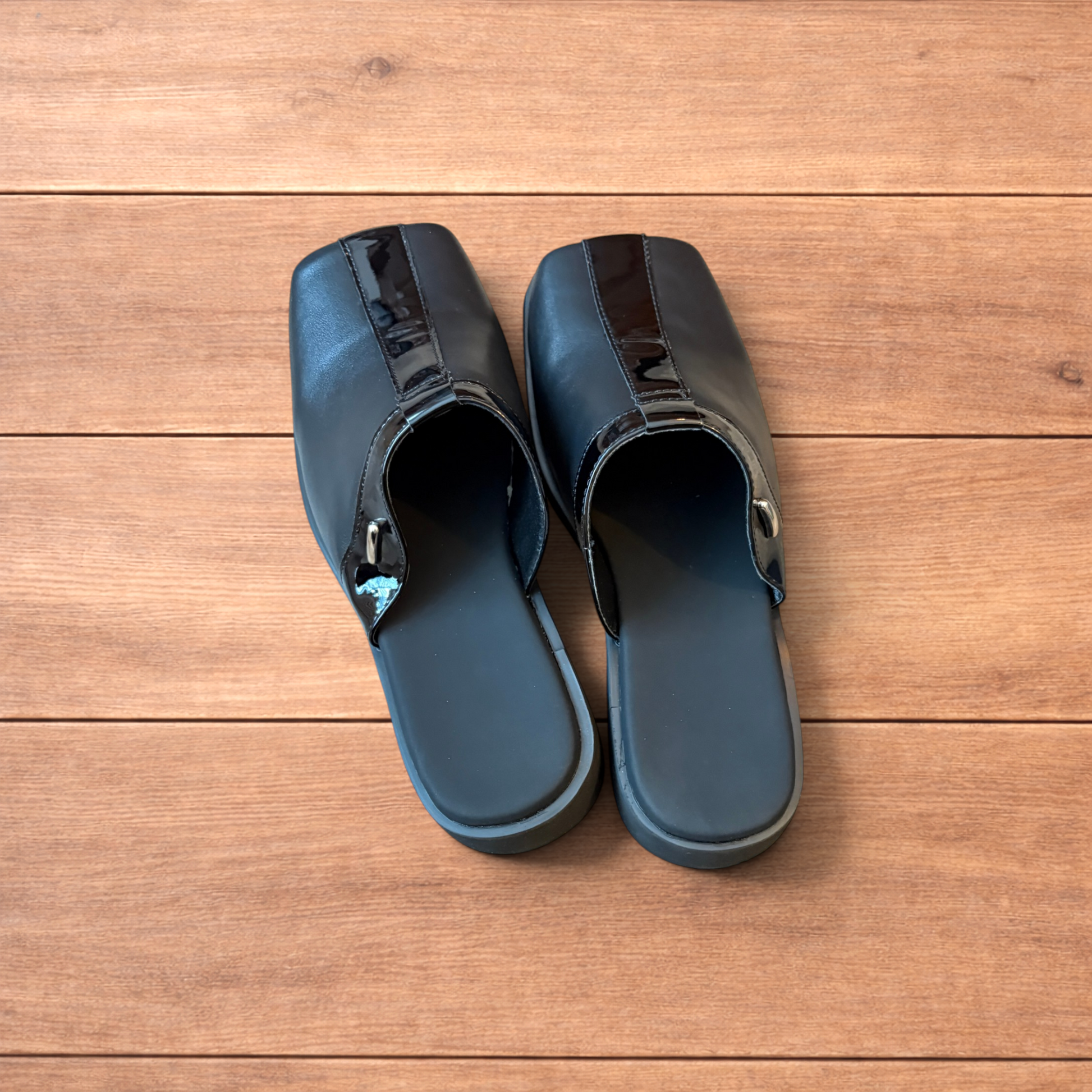 Pair of black faux leather slip on clogs with matte and patent panels and rubber heels on wooden floor