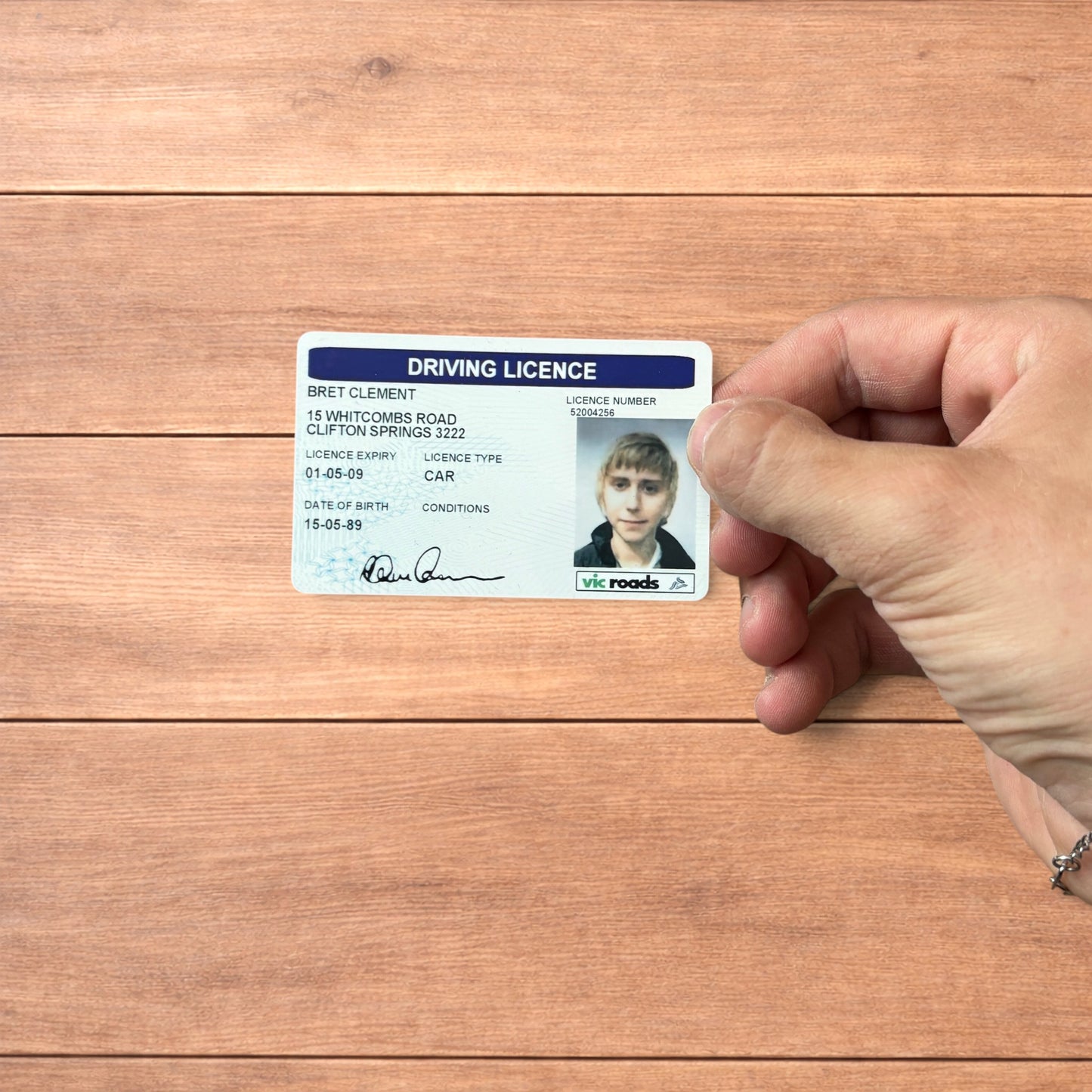 Brett Clement driving licence novelty card with blue header and photo ID, shown front and back and held in hand.