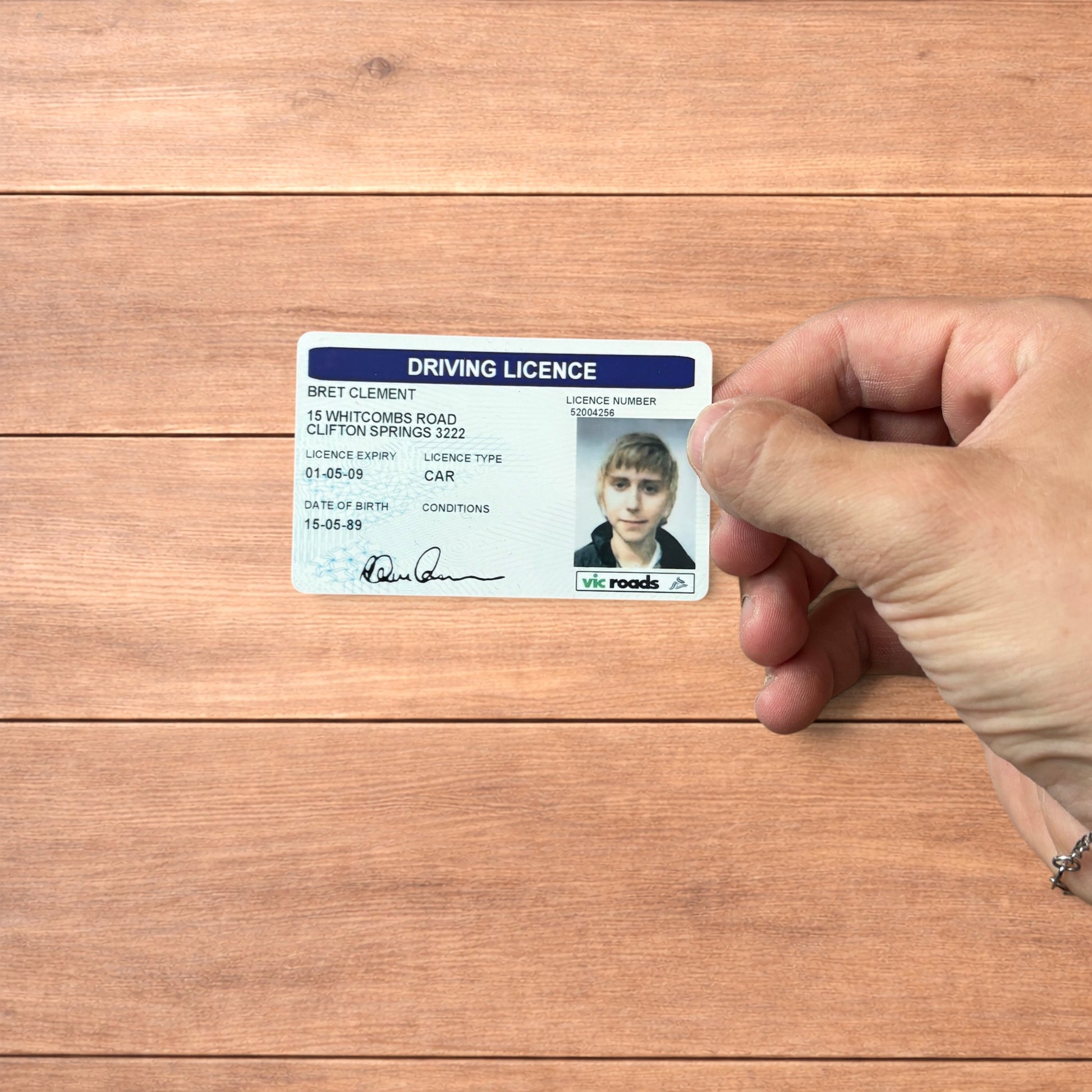 Brett Clement driving licence novelty card with blue header and photo ID, shown front and back and held in hand.