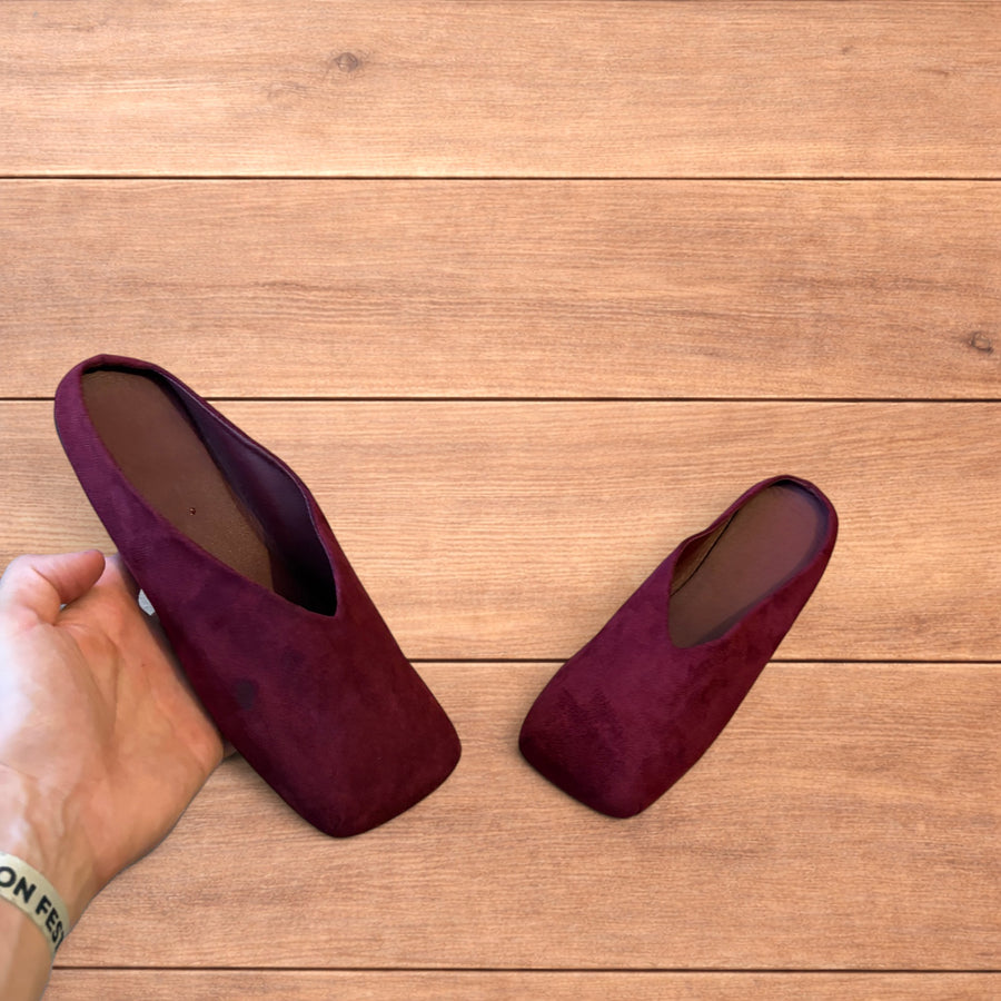 Pair of vintage style red suede flat top square toe slip-on shoes on wooden floor