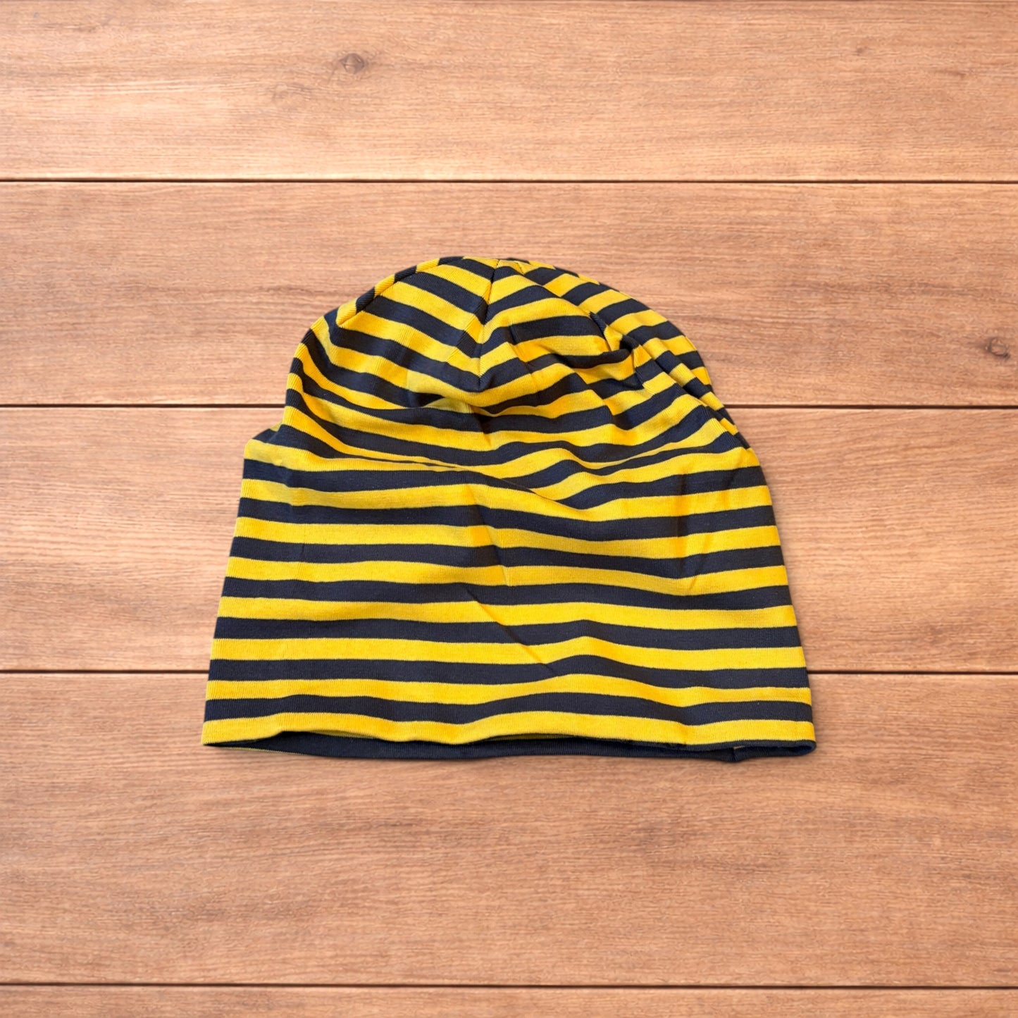 Vintage style striped beanie hat in yellow and black laid flat on wooden surface