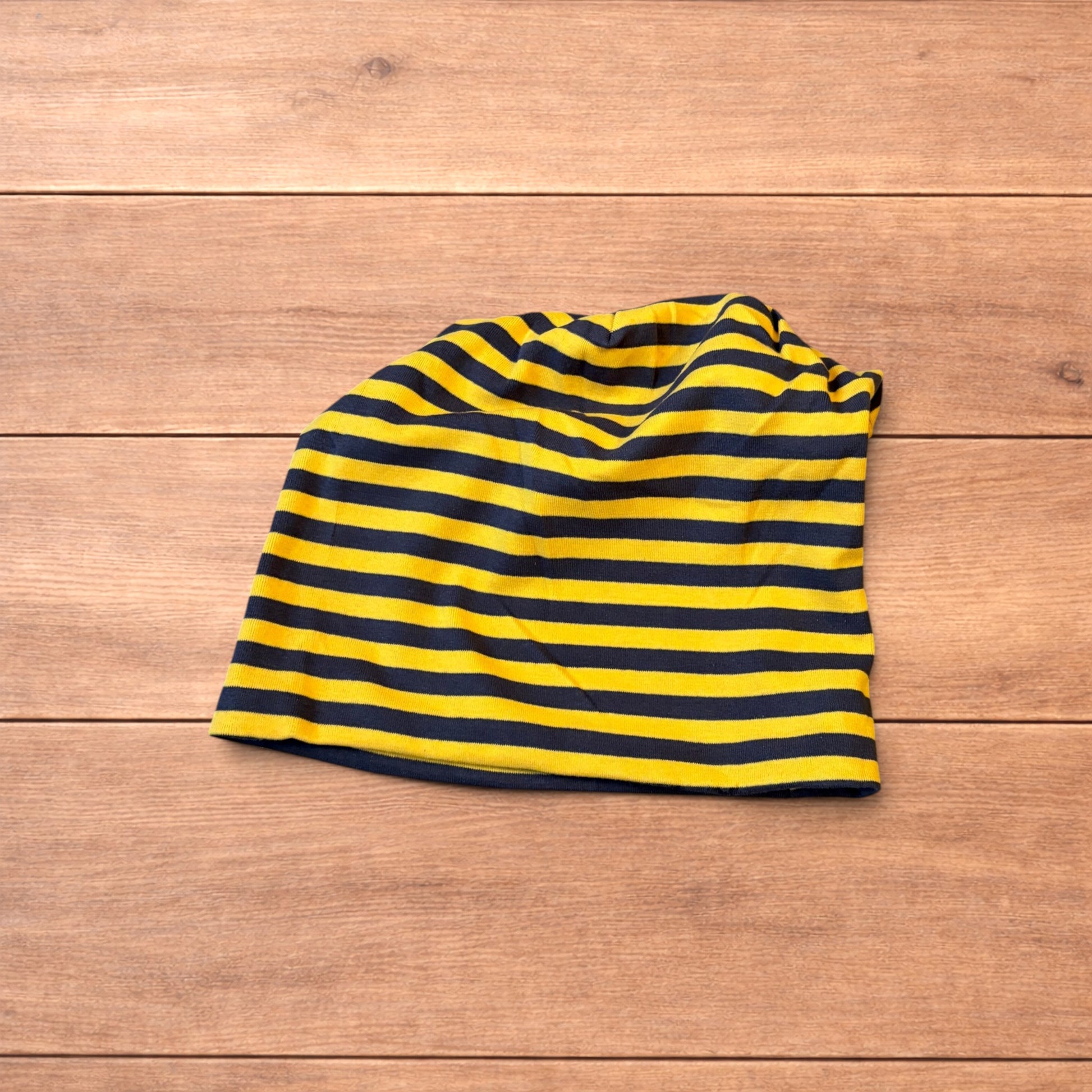 Vintage style striped beanie hat in yellow and black laid flat on wooden surface