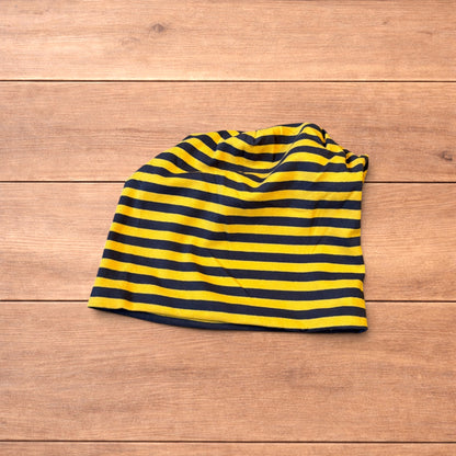 Vintage style striped beanie hat in yellow and black laid flat on wooden surface