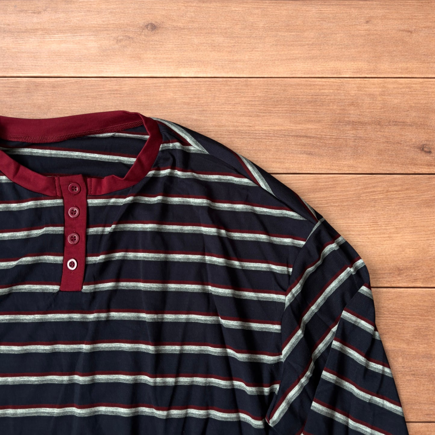Navy navy blue striped henley long sleeve top with burgundy collar and button placket laid flat on wooden background