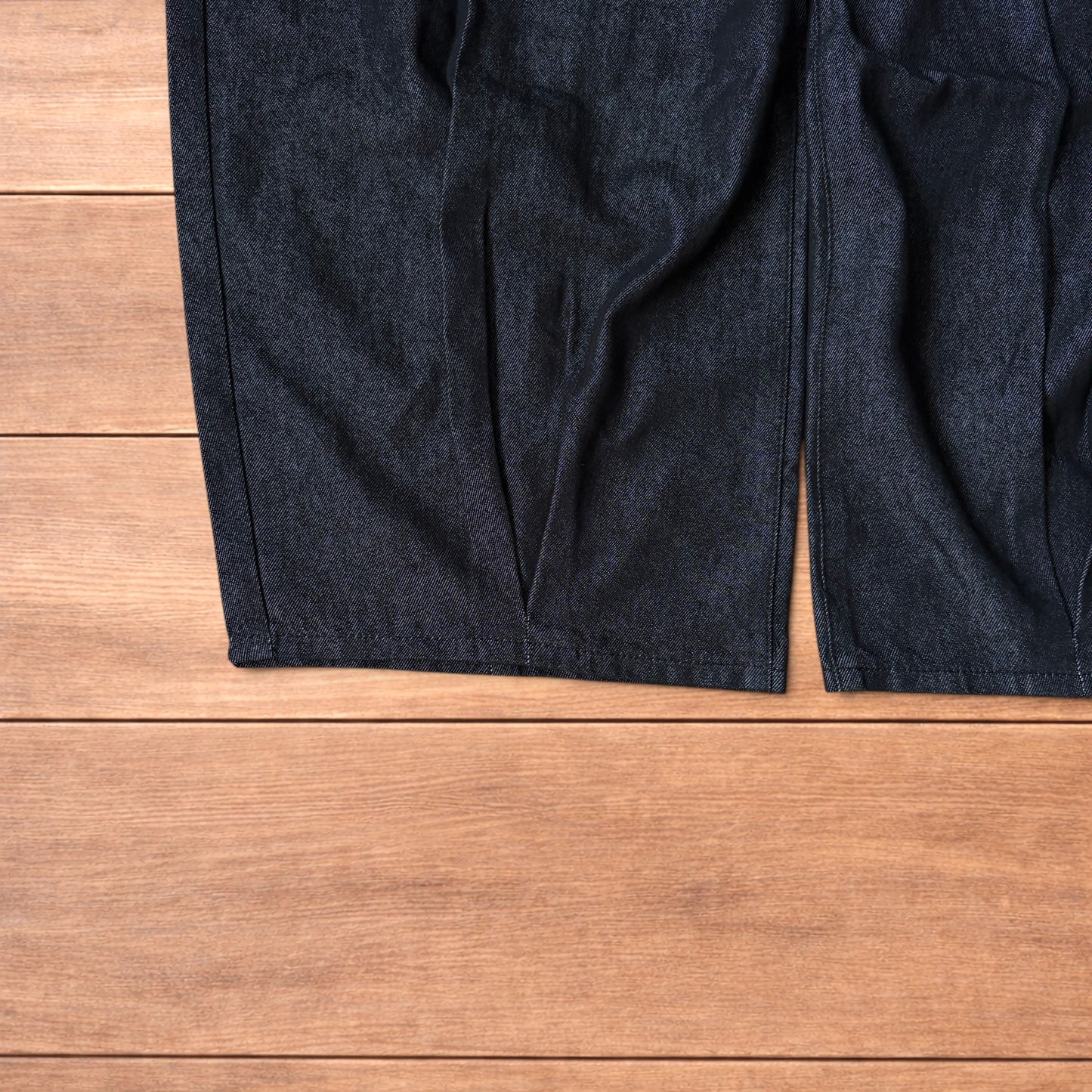 Dark grey baggy wide leg raw denim jeans laid flat showing front and back pockets and button fly