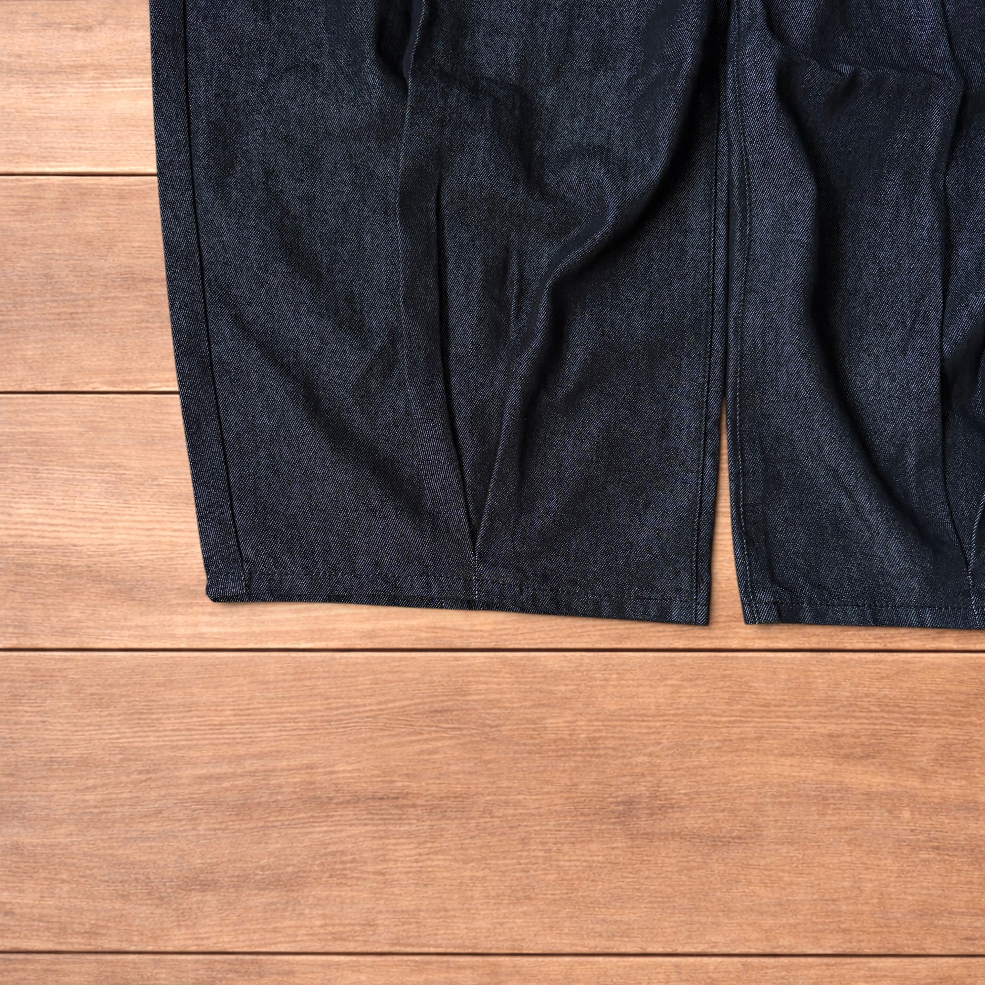 Dark grey baggy wide leg raw denim jeans laid flat showing front and back pockets and button fly